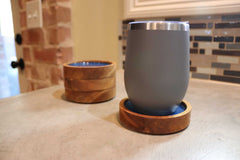 A sleek gray smoothie cup sits on a Willy's Woods Customized Round Cedar Coaster, expertly crafted from premium cedar wood, with another coaster nearby. In the background, a tiled wall and red brick section create a warm kitchen setting.