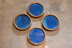 Four Customized Round Cedar Coasters by Willy's Woods, with blue ceramic centers, are elegantly arranged on a concrete surface.