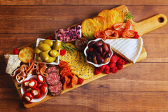 Discover Willy's Woods' Customizable Maple & White Oak Layered Wooden Charcuterie Boards, adorned with cheeses, olives, cured meats, crackers, raspberries, and stuffed peppers. This colorful gift features rosemary sprig garnishes and can include engraved text for a personalized touch.